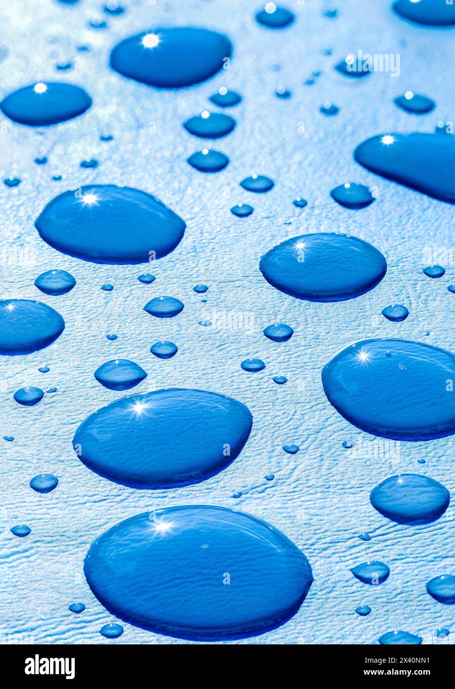 Nahaufnahme großer Wassertröpfchen auf blauem Hintergrund mit einem Sonnenstrahl in den Wassertröpfchen; Studio Stockfoto