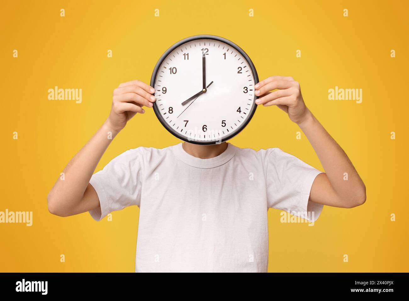 Teenager, der sein Gesicht mit großer Uhr bedeckt, orangefarbenes Panorama Stockfoto