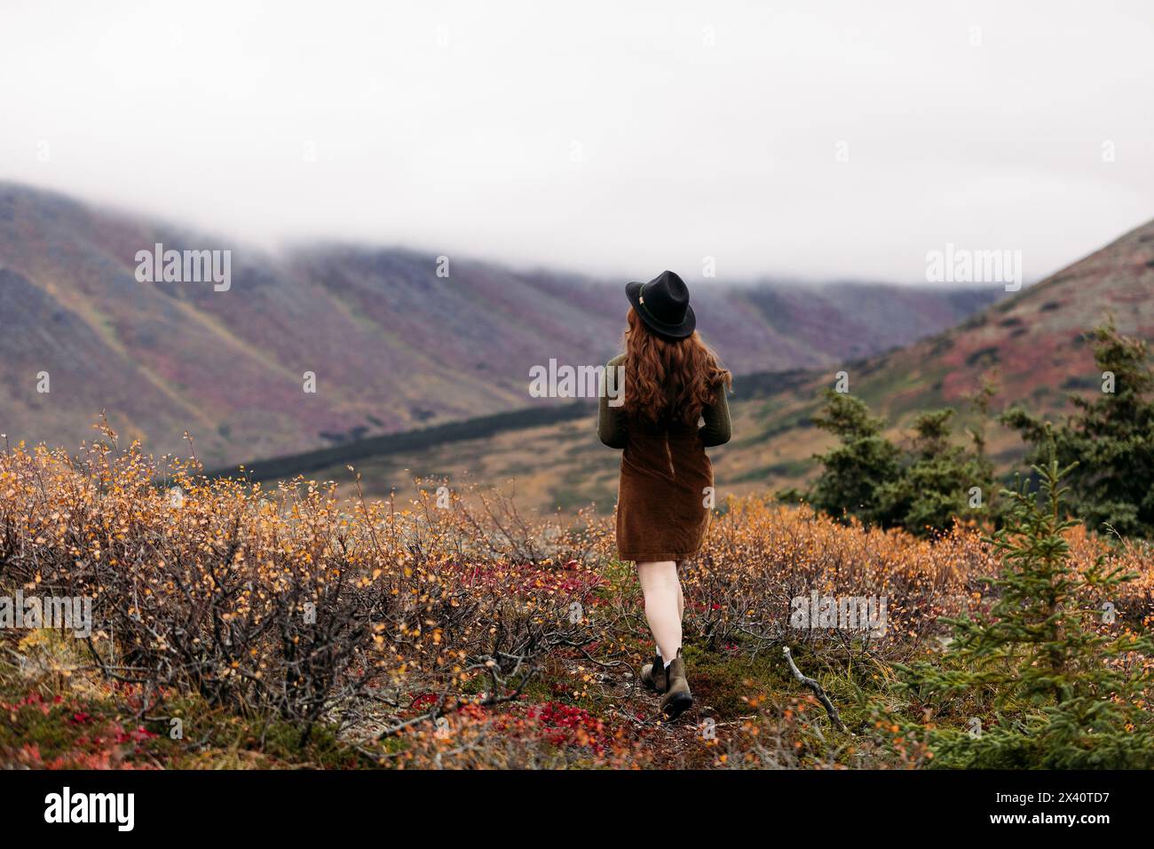 Blick von hinten auf ein Teenager-Mädchen mit schwarzem Hut und braunem Pullover, das im Herbst in den Glen Alps spaziert Stockfoto