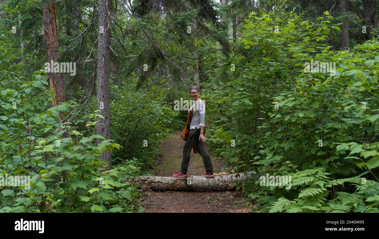 Die Frau balanciert auf einem Baumstamm über einen Wanderweg in einem Wald, Boyne Lake Trail; Ontario, Kanada Stockfoto
