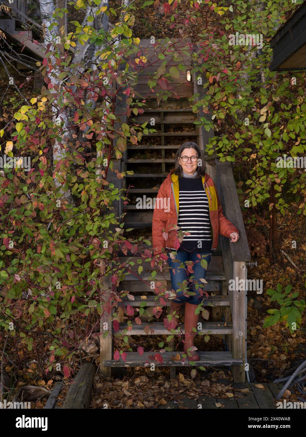Frau steht auf Holztreppen im Freien, umgeben von Herbstlaub; Lake of the Woods, Ontario, Kanada Stockfoto