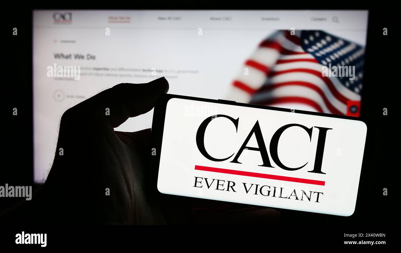 Person mit Smartphone und Logo des US-amerikanischen IT-Unternehmens CACI International Inc. Vor der Website. Schwerpunkt auf dem Display des Telefons. Stockfoto