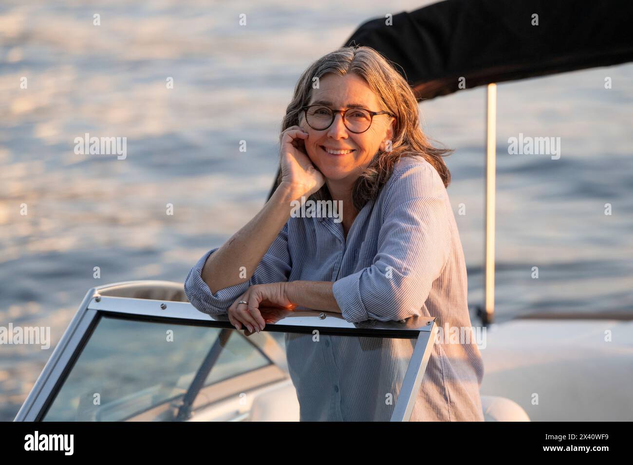 Informelles Außenporträt einer Frau in einem Schnellboot in der warmen Dämmerung; Lake of the Woods, Ontario, Kanada Stockfoto