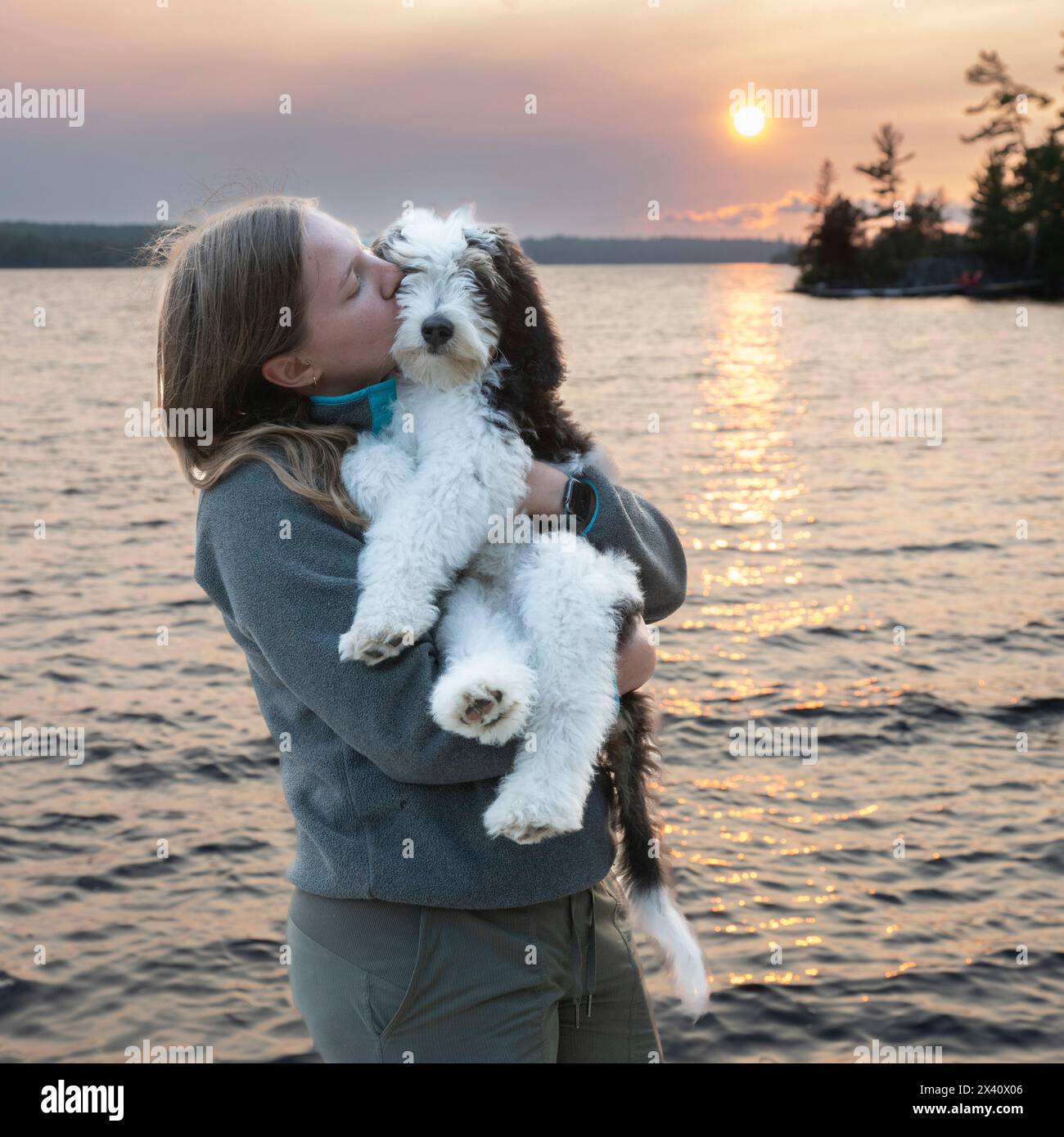 Mädchen zeigt Zuneigung zu ihrem Hund auf einem See bei Sonnenuntergang; Lake of the Woods, Ontario, Kanada Stockfoto
