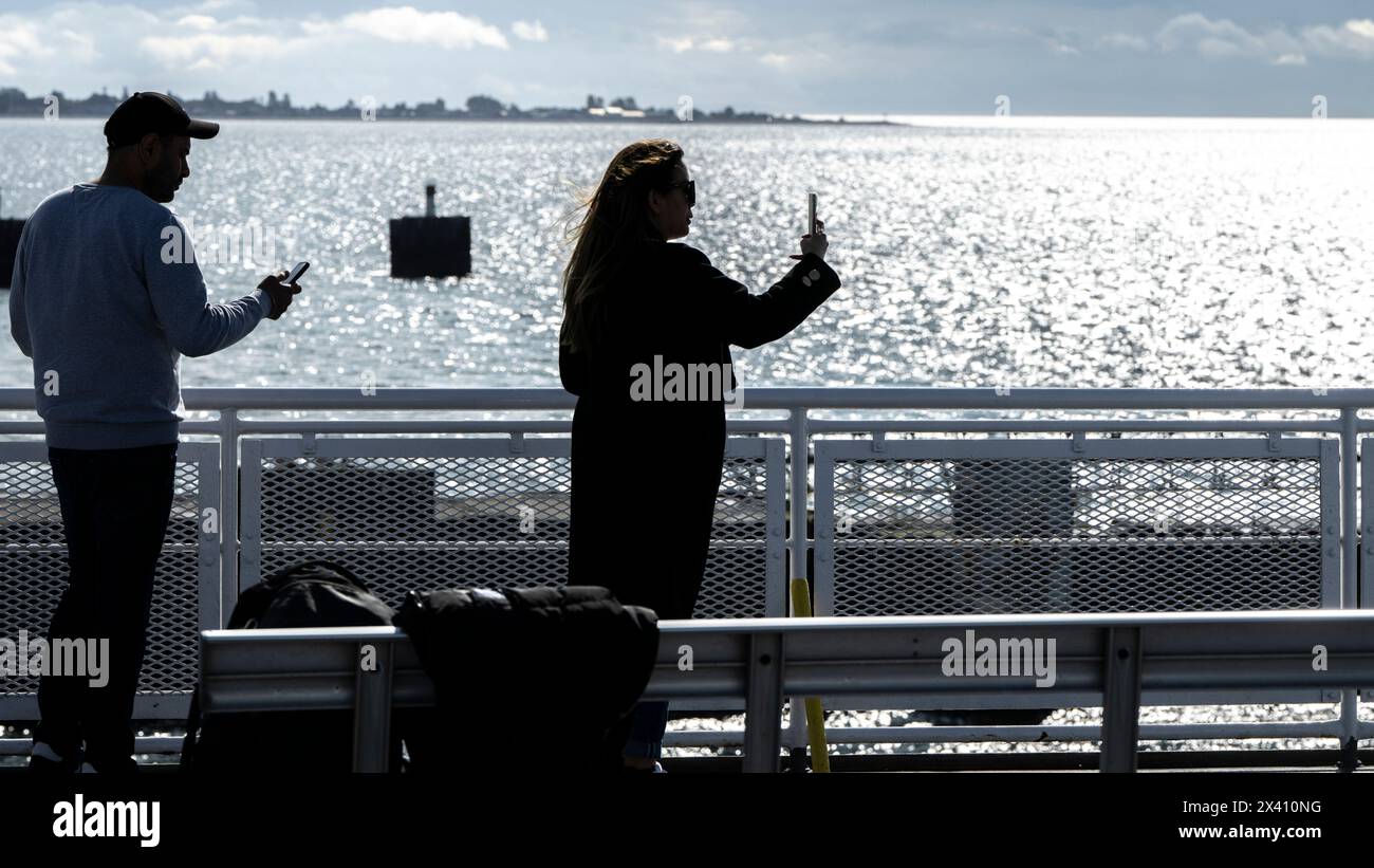 Die Menschen stehen und fotografieren den schimmernden Blick auf das Meer und die Küste mit ihren Smartphones vom Deck einer Fähre aus: British Columbia, Kanada Stockfoto