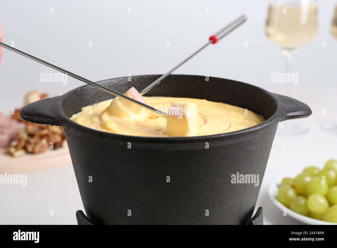 Schinken in Fonduekanne mit leckerem geschmolzenem Käse am Tisch, Nahaufnahme Stockfoto