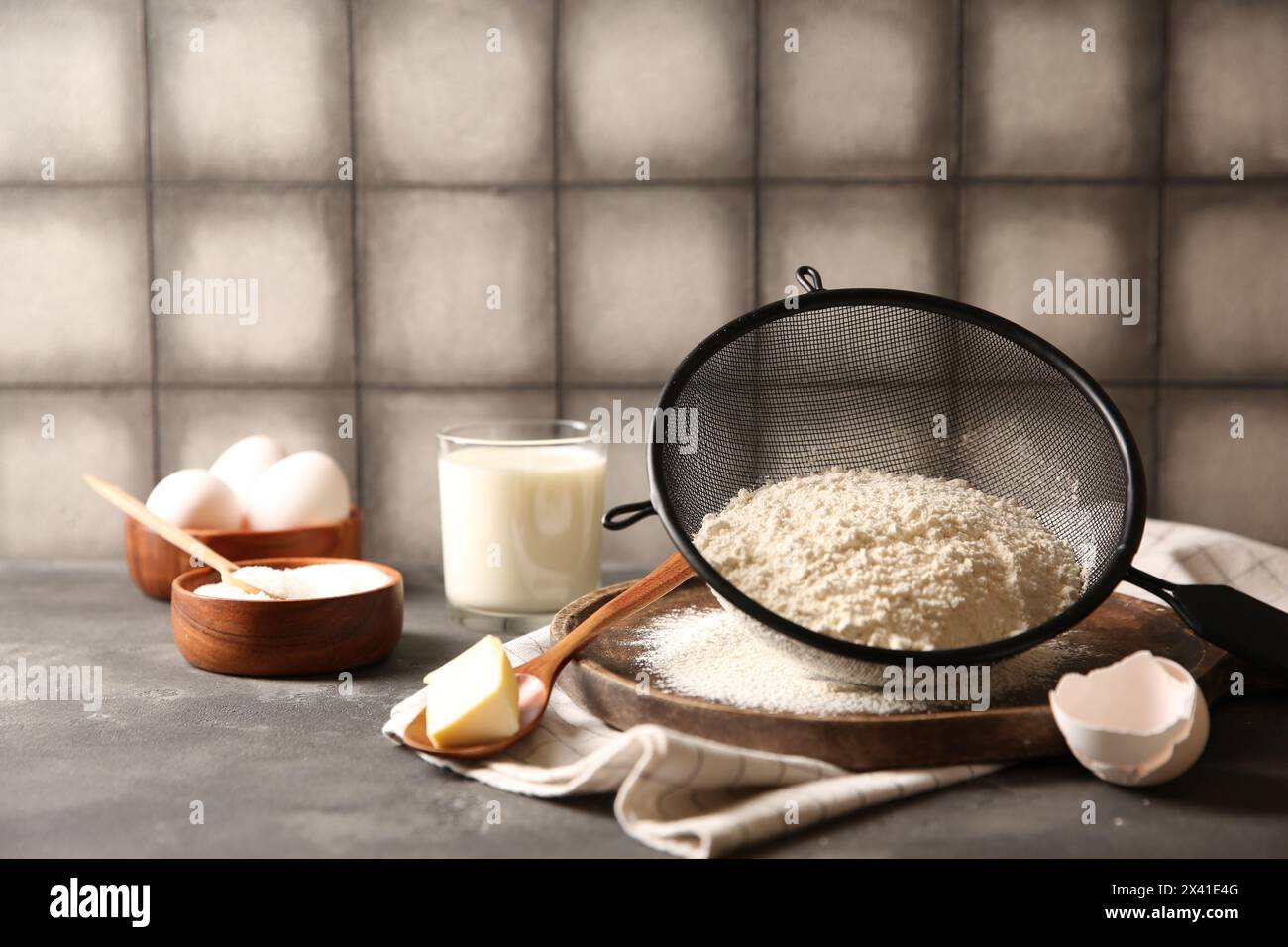 Teig herstellen. Mehl im Sieb, Löffel und Butter auf grauem Tisch, Nahaufnahme Stockfoto