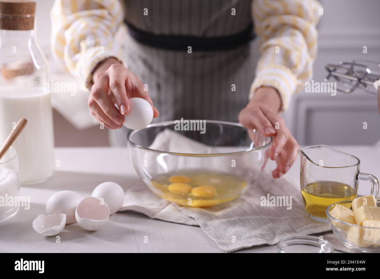 Teig herstellen. Frau bricht Ei am weißen Tisch in der Küche, Nahaufnahme Stockfoto