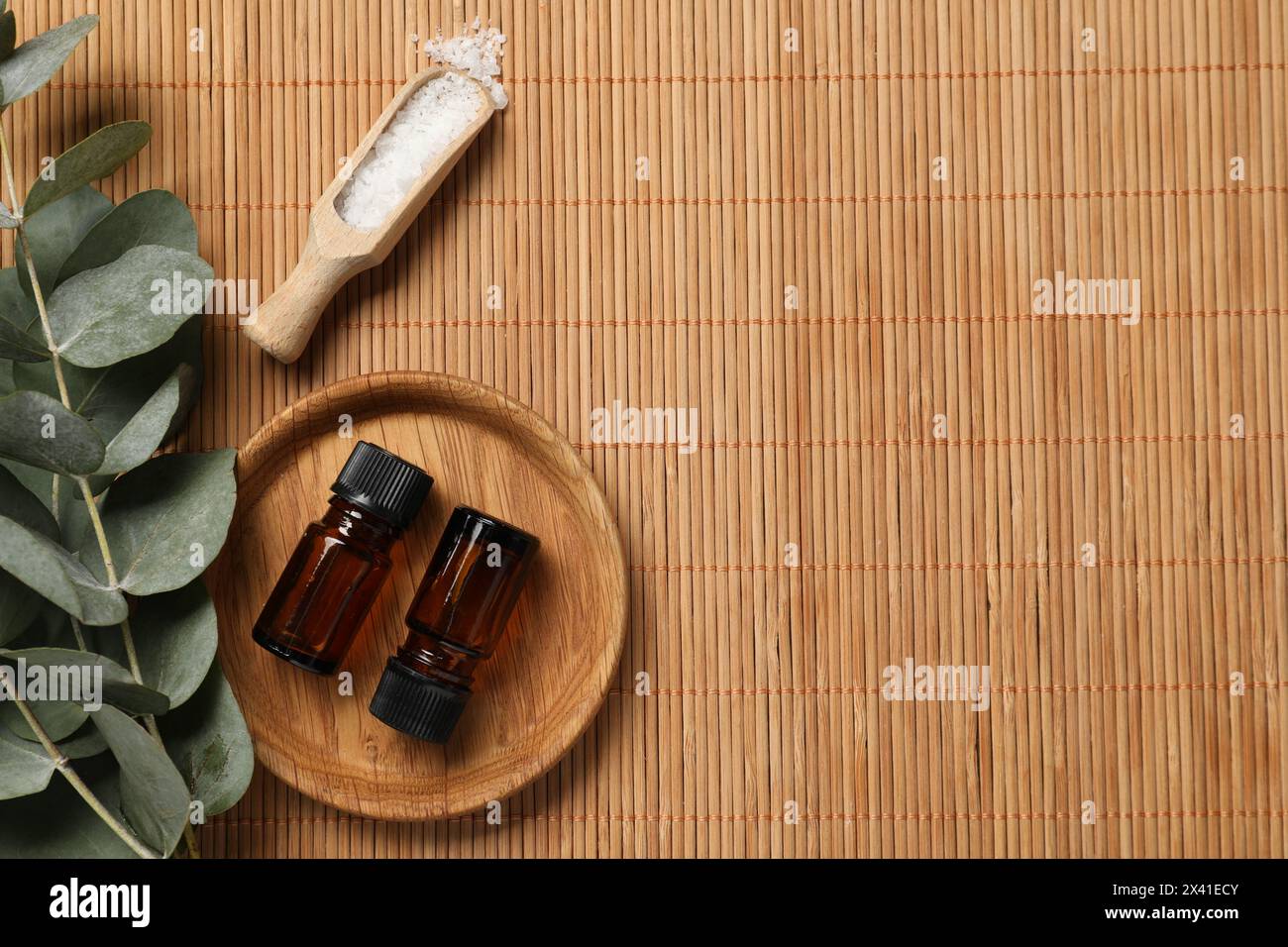 Aromatherapieprodukte. Flaschen mit ätherischem Öl, Meersalz und Eukalyptuszweigen auf Bambusmatte, flach liegend. Leerzeichen für Text Stockfoto