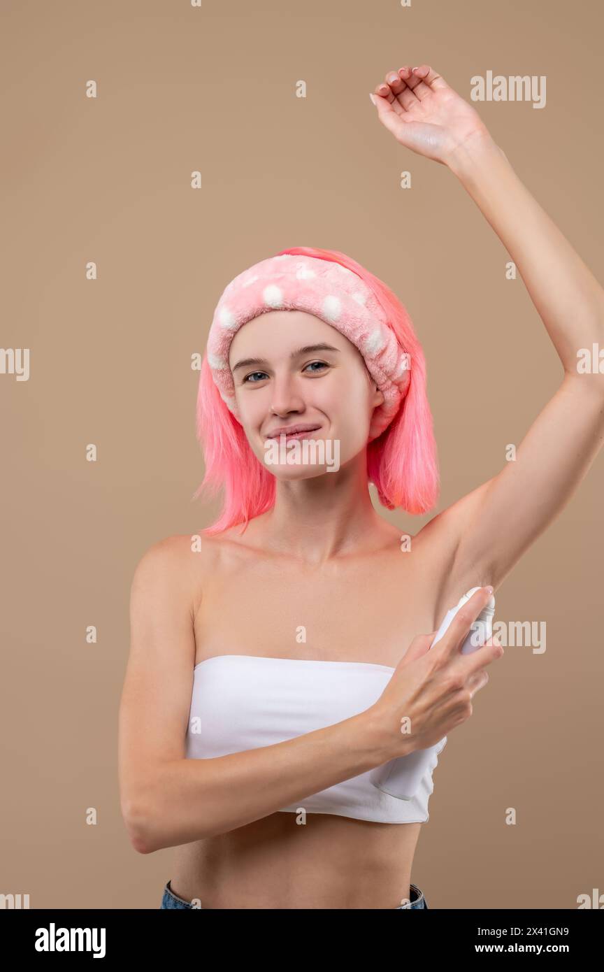 Rosafarbene junge Frau, die Deodorant auf ihren Körper sprüht Stockfoto