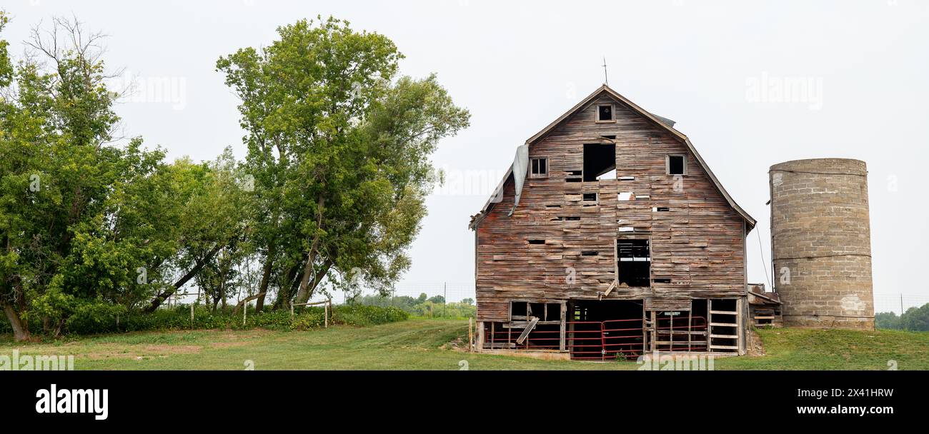 Old Farm Barn und Silo in schlechtem Zustand und Bäume und Zaun mit bedecktem Himmel im Norden von Minnesota Stockfoto