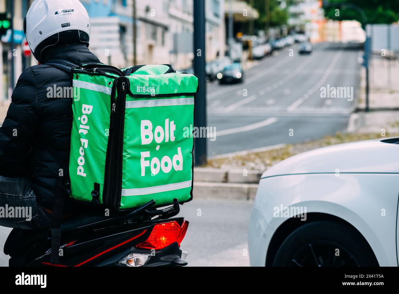 Lissabon, Portugal - 28. April 2024: Der Fahrer von Bolt Food, der einen hellgrünen, isolierten Rucksack trägt, wird von hinten gesehen, während er an der Seite wartet Stockfoto