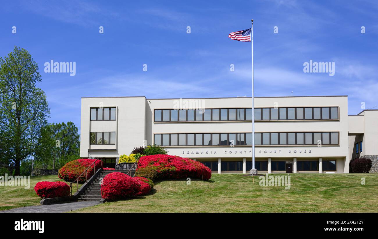 Stevenson, WA, USA - 23. April 2024; Gebäude des Skamania County Court House mit Frühlingsroten Pflanzen und amerikanischer Flagge Stockfoto