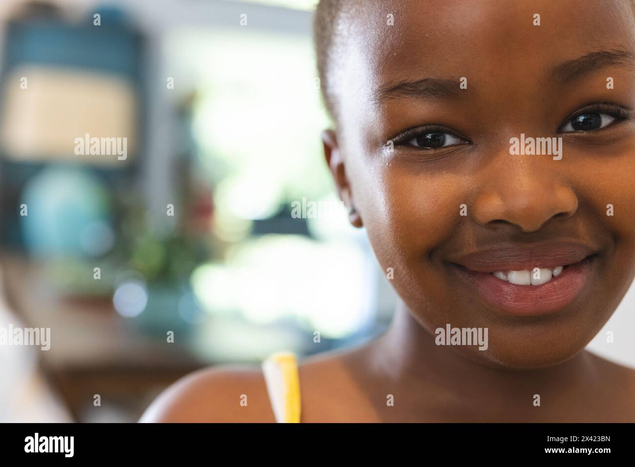 Zu Hause, ein junges afroamerikanisches Mädchen mit gelbem Strohhalm, hell lächelnd, Kopierraum Stockfoto