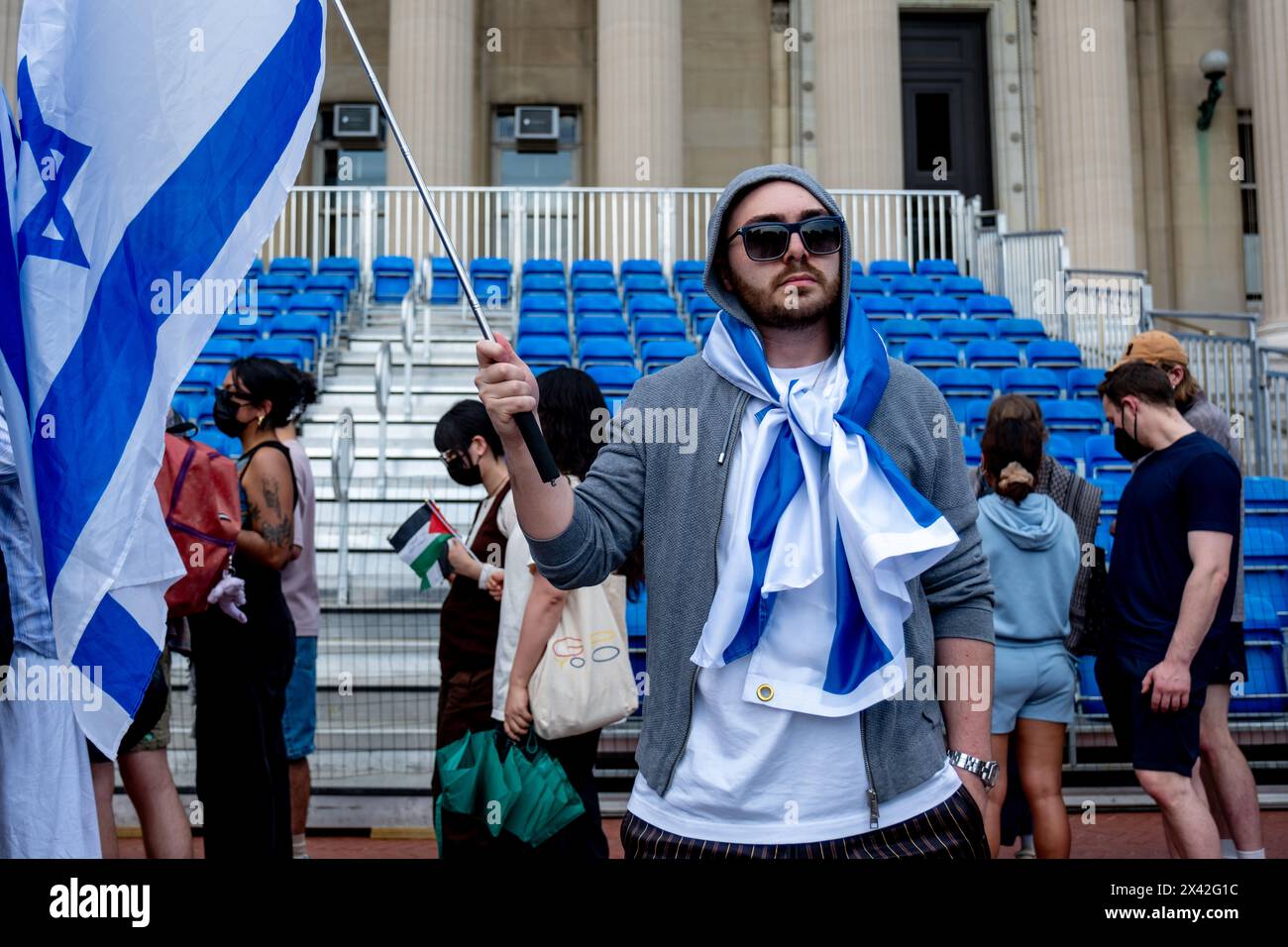 New York, Usa. April 2024. Ein Student steht auf der Treppe vor der Low Memorial Library mit Isreali-Flagge, während Pro-Palästina-Demonstranten hinter ihm marschieren. Pro-Palästina-Studenten, die im „Gaza Solidarity Encamp“ auf dem Gelände der Columbia University lebten, wurden bis heute 14:00 Uhr zur Räumung oder zur Aussetzung gegeben. Als Zeichen der Unterstützung marschierten Hunderte von Kolumbien über den Campus und forderten die Universität auf, die finanziellen Beziehungen zu Israel und zum „freien Palästina“ zu unterbrechen. Quelle: SOPA Images Limited/Alamy Live News Stockfoto