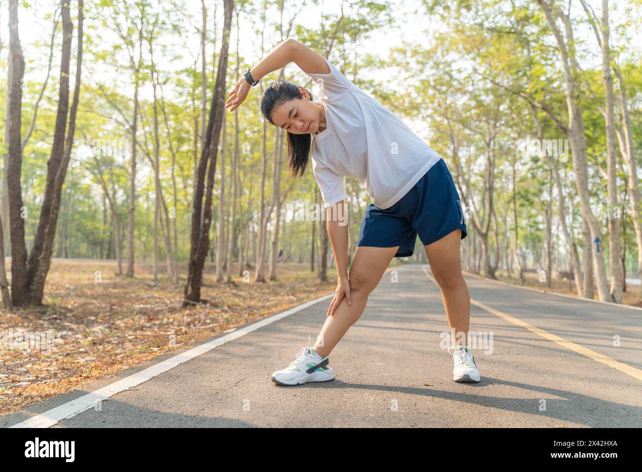 Junge Läuferin, die ihre Arme und Beine ausdehnt, bevor sie ihren morgendlichen Lauf in einem örtlichen Laufpark beginnt Stockfoto