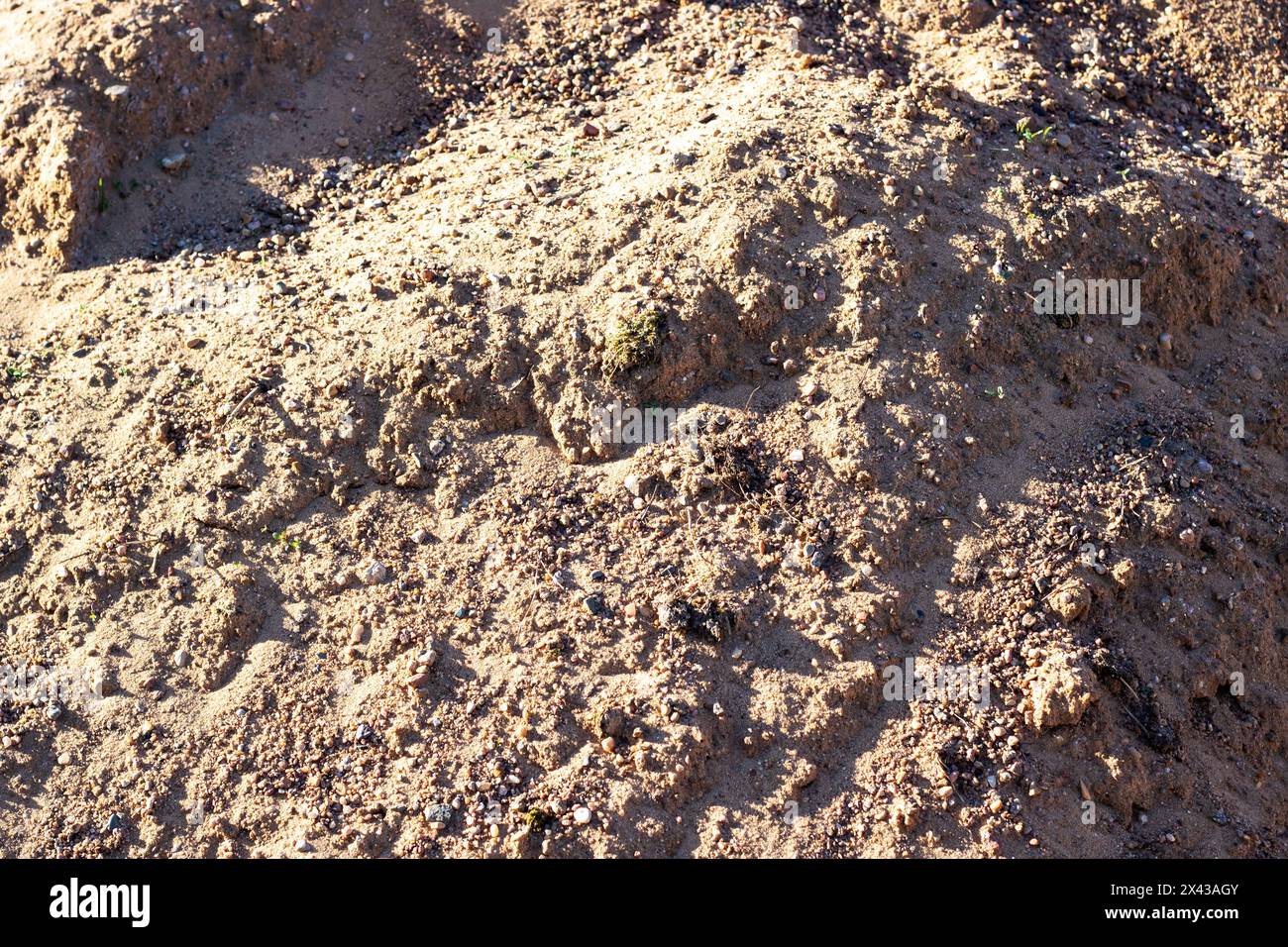 Eine Mischung aus Boden, braunem Grundgestein und kleinen Felsen, die einer Mini-Landschaft ähneln. Das Gesteinsmuster schafft einen interessanten Kontrast im grasbewachsenen Bereich Stockfoto