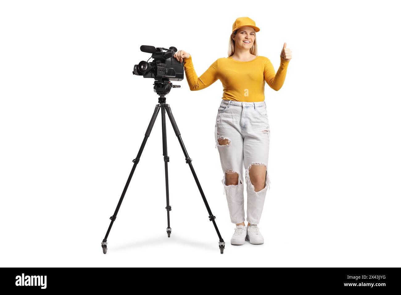 Porträt einer Kamerabedienerin in voller Länge mit einer Kamera auf einem Stativstativ, die Daumen isoliert auf weißem Hintergrund nach oben bewegt Stockfoto