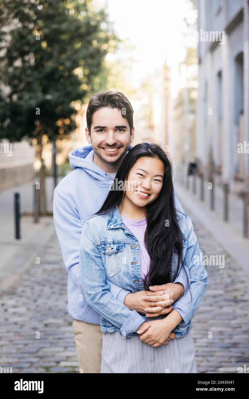 Fröhlicher Mann umarmt seine Freundin von hinten, während er im Freien steht. Pärchen genießen sich im Freien. Stockfoto
