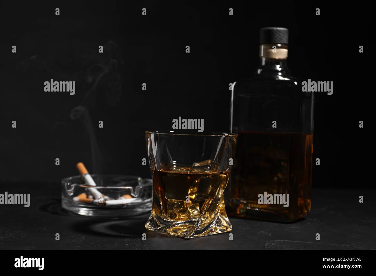 Alkoholsucht. Whiskey, schwelende Zigaretten und Aschenbecher auf dunkel strukturiertem Tisch Stockfoto