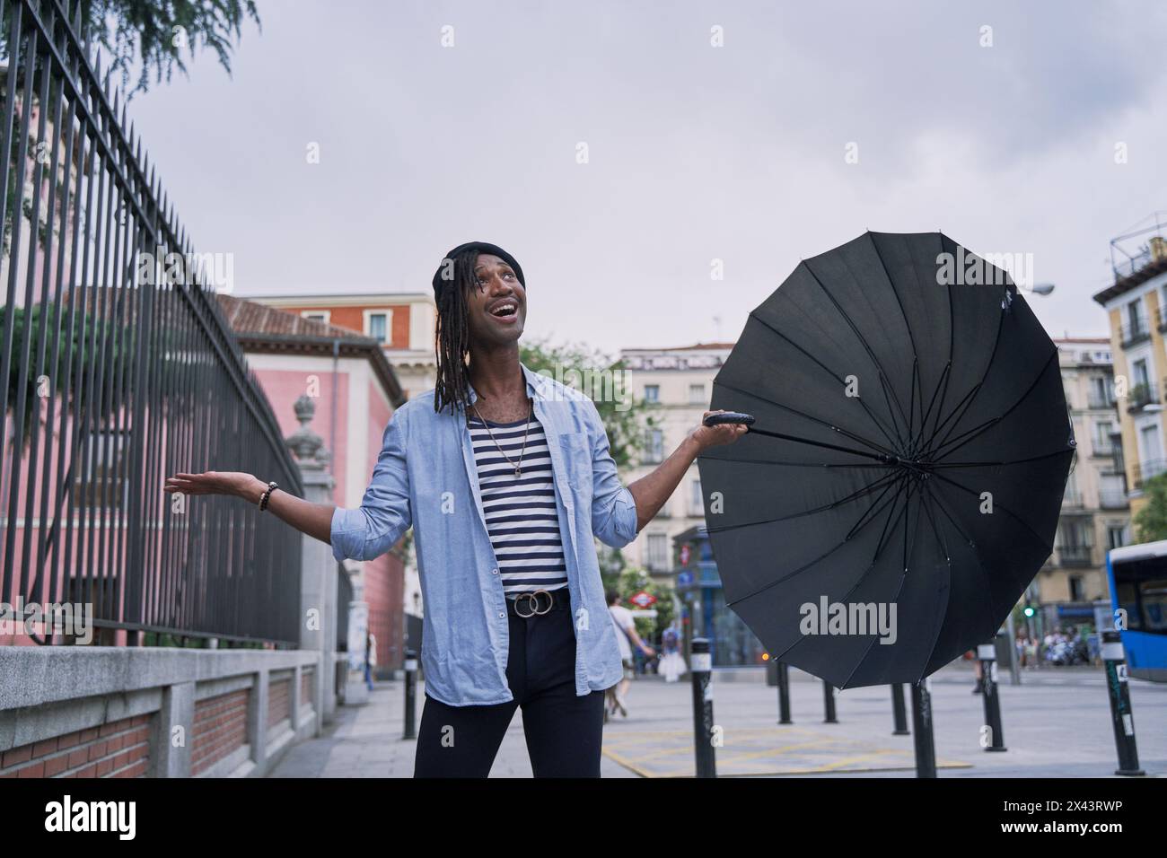 Attraktiver afrikanischer Mann mit Regenschirm, der ihn aushält, um zu sehen, ob es regnet Stockfoto