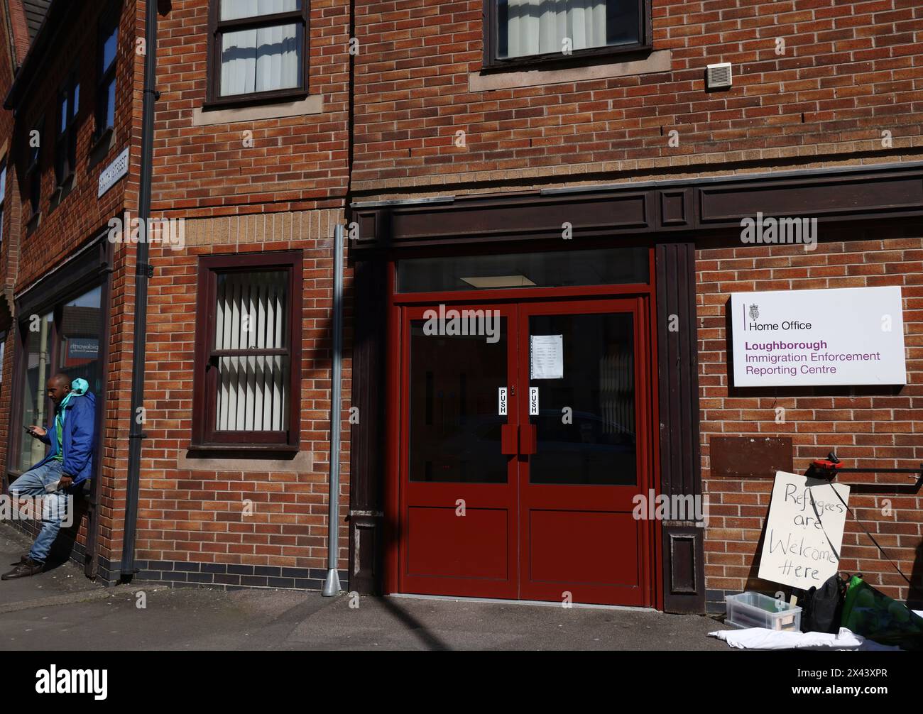 Loughborough, Leicestershire, Großbritannien. 30. April 2024. Ein Mann wartet auf den Eintritt in ein Meldezentrum für Einwanderungsbehörden, während Demonstranten gegen die geplante Deportation von Migranten und Flüchtlingen nach Ruanda protestieren. Credit Darren Staples/Alamy Live News. Stockfoto