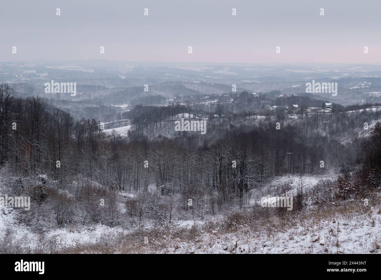 Hügelige Winterlandschaft mit Wald und verstreuten Dörfern, ruhige Landschaft an bewölkten, langweiligen Tagen Stockfoto