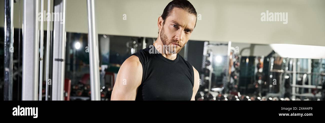 Ein fitter Mann in einem schwarzen Tanktop führt Übungen in einem gut ausgestatteten Fitnessstudio durch, wobei er sich auf Kraft- und Ausdauertraining konzentriert. Stockfoto