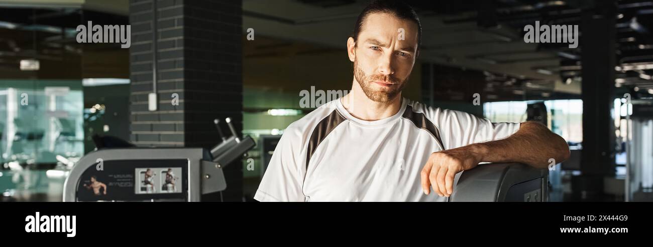 Ein fitter Mann in sportlicher Kleidung, der neben einer Maschine in einem Fitnessstudio steht. Stockfoto
