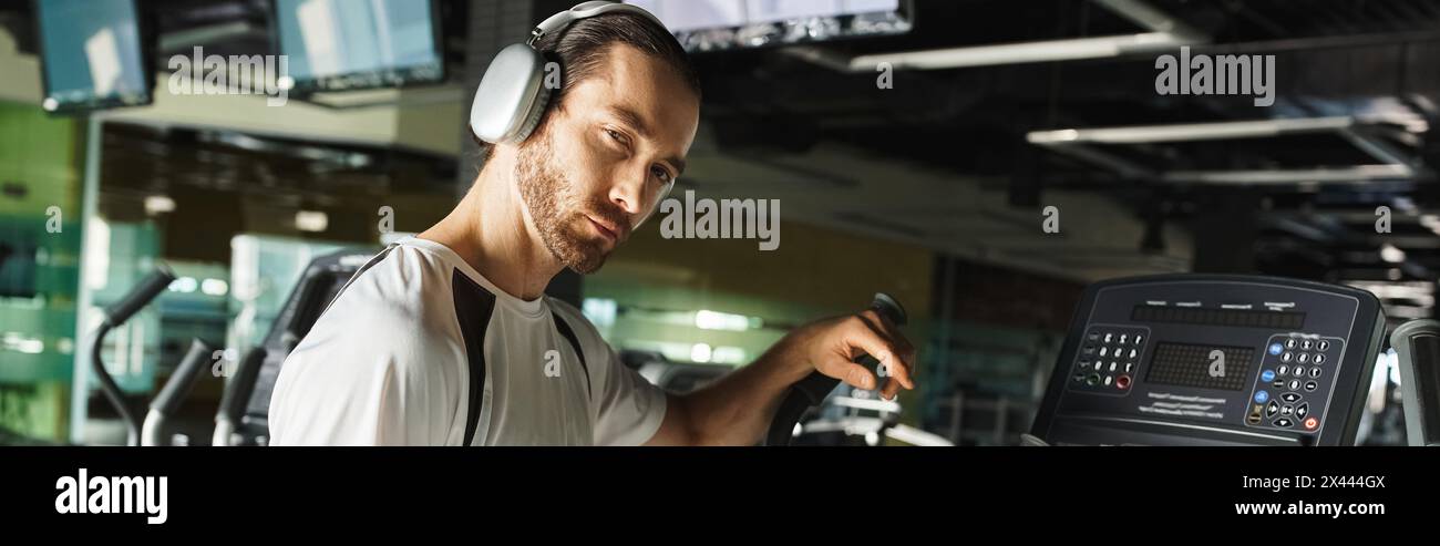 Ein sportlicher Mann in aktiver Kleidung verwendet ein Gerät, während er Kopfhörer trägt, um ein Workout mit Musik zu genießen. Stockfoto