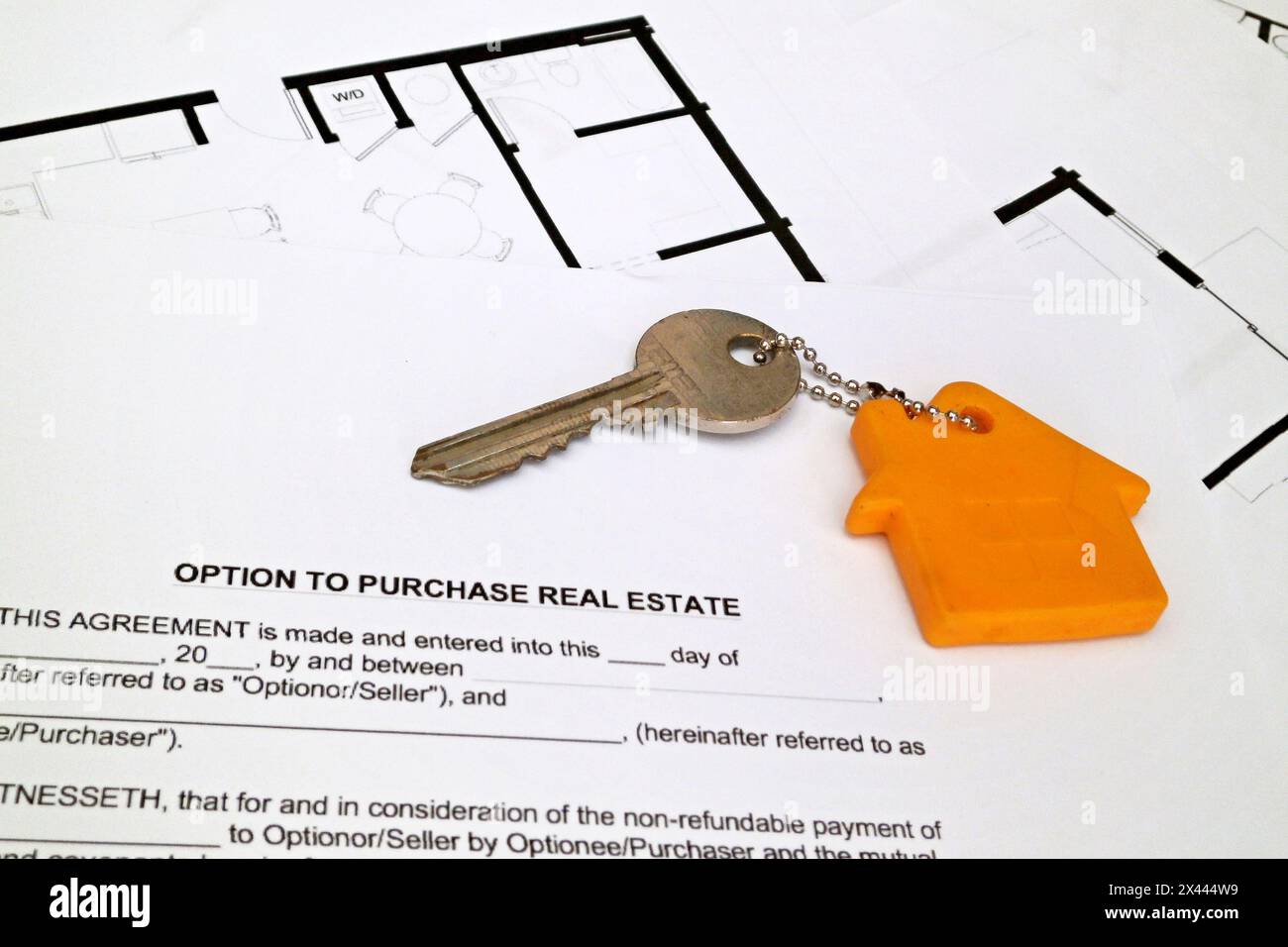 Nahaufnahme eines Schlüssels, der am Schlüsselring angebracht ist, auf der Oberseite einer Option zum Kauf von Immobilien und Bauplänen. Stockfoto