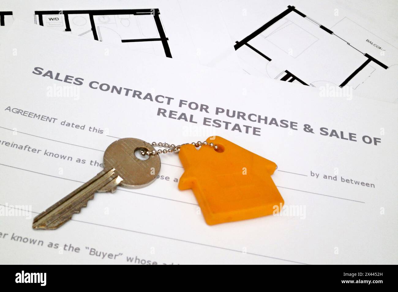 Nahaufnahme eines Schlüssels, der am Schlüsselring oben auf einem Kaufvertrag für den Kauf und Verkauf von Immobilien und Bauplänen befestigt ist. Stockfoto