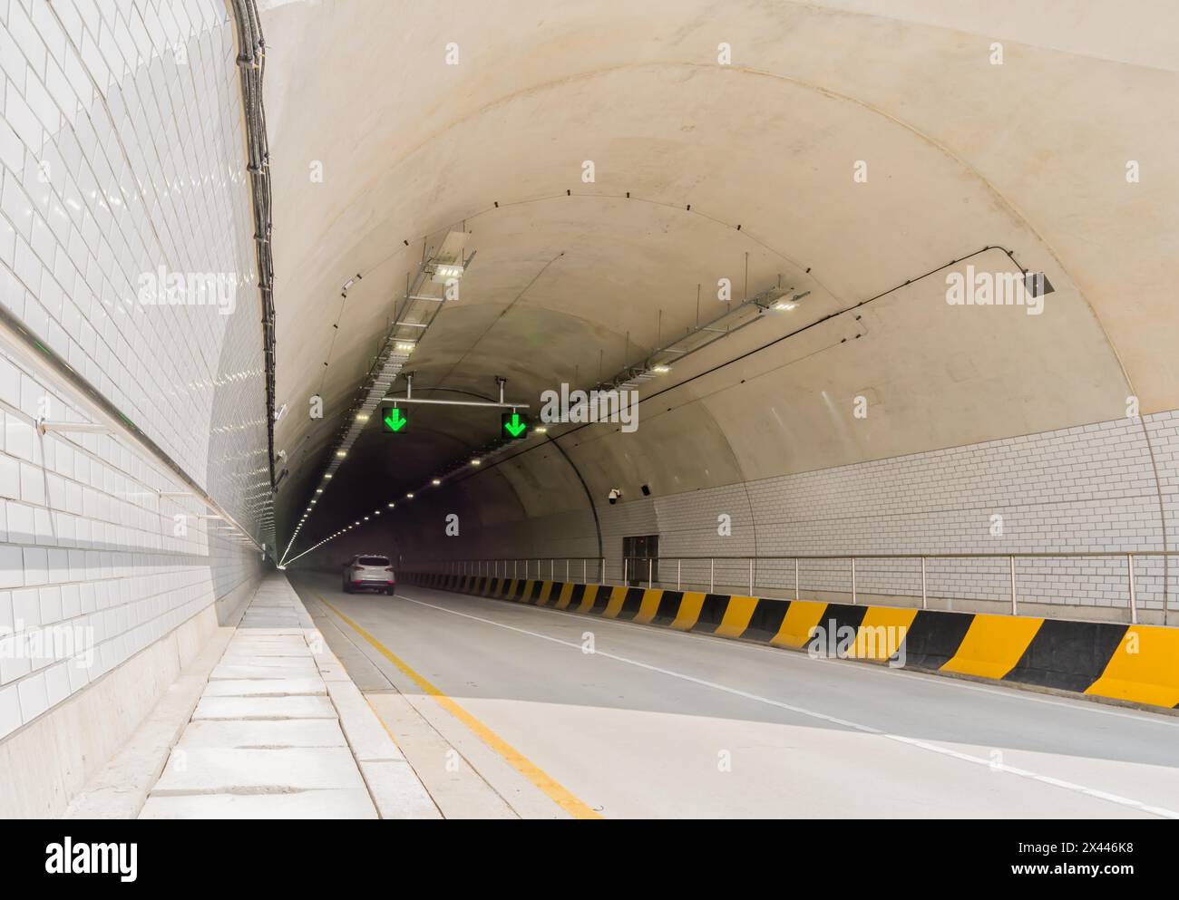 Zweispuriger Autobahntunnel aus weißem Beton mit Leuchtstofflampen und grünen Pfeilen an der Decke und Stromkabeln, die an der Seitenwand hinunter laufen Stockfoto