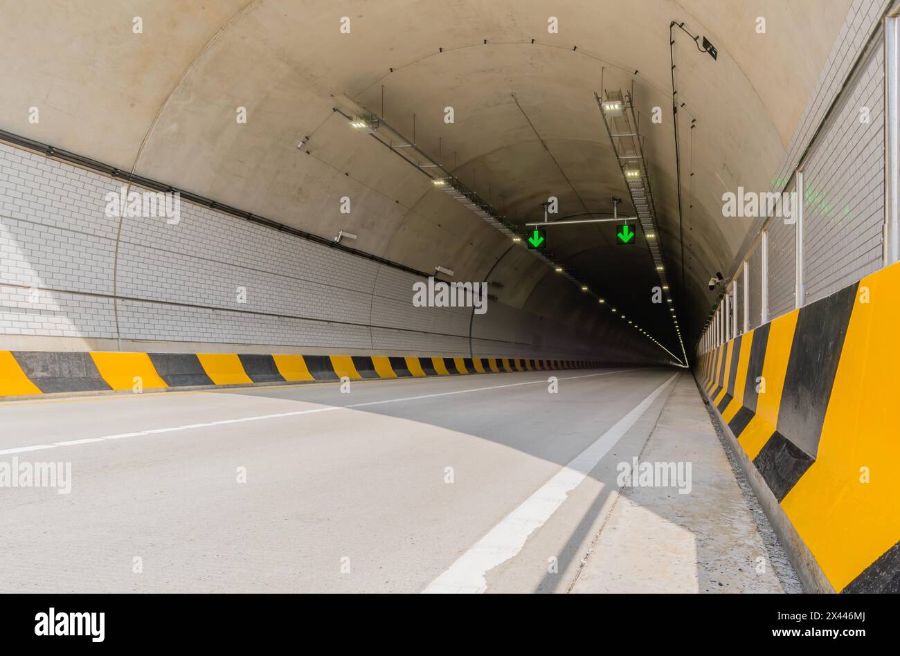 Zweispuriger Autobahntunnel aus weißem Beton mit Leuchtstofflampen und grünen Pfeilen an der Decke und Stromkabeln, die an der Seitenwand hinunter laufen Stockfoto