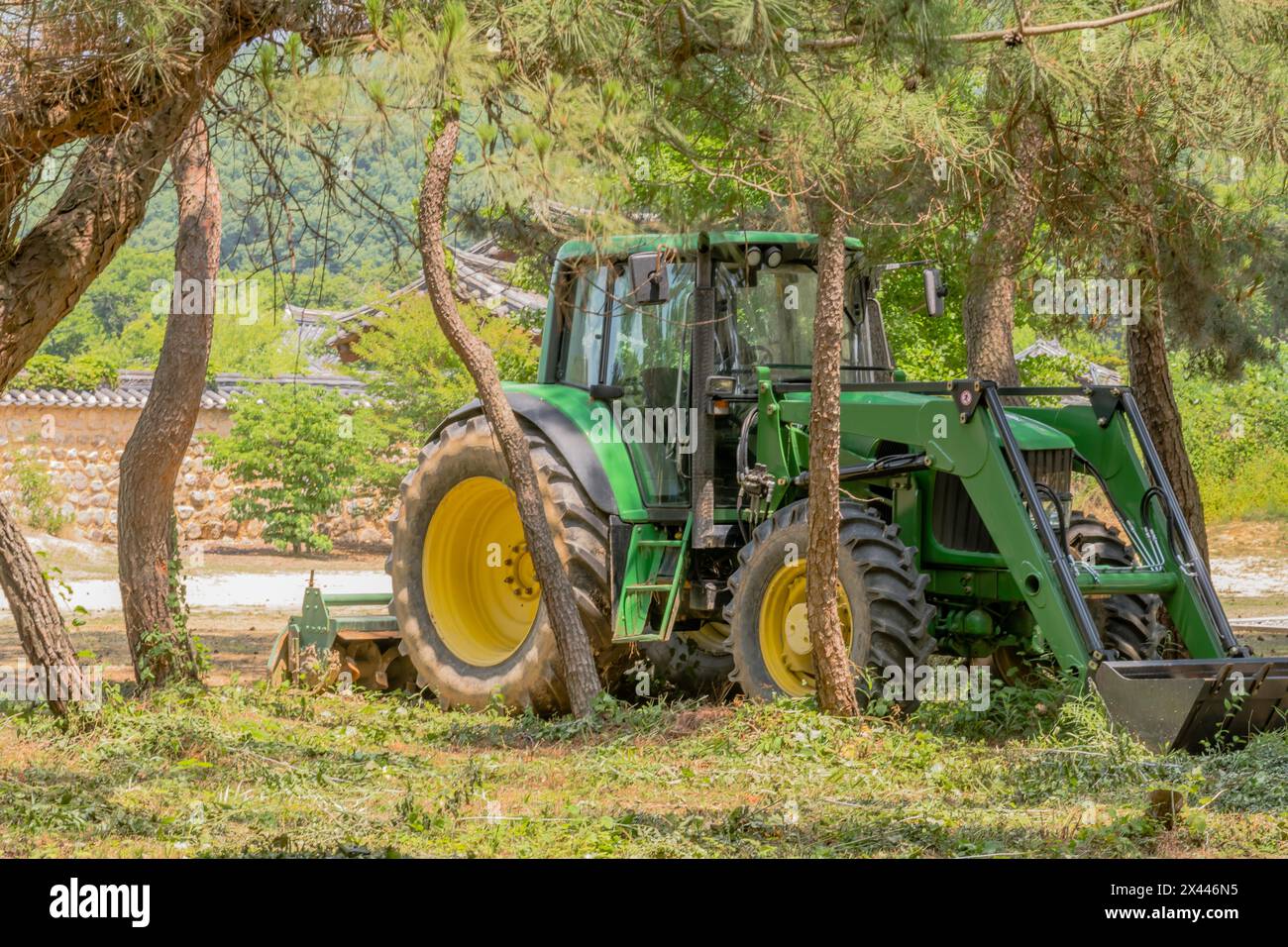Grüner Traktor mit gelben Rädern, der im Schatten eines Baumhains in Südkorea geparkt ist Stockfoto