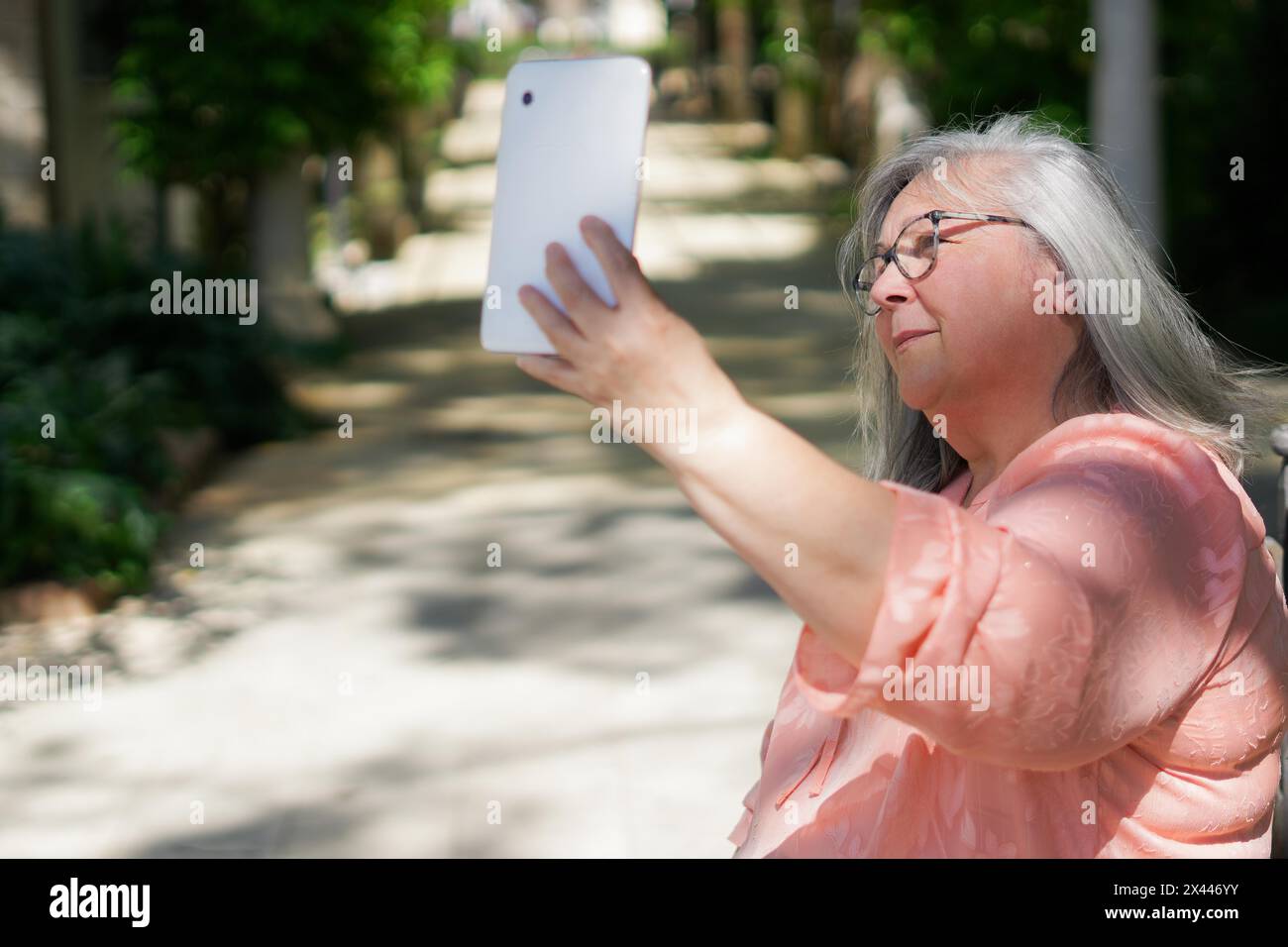 Positive alte Dame macht Selfie im Park. Ältere grauhaarige Frau in lässiger Haltung Gadget mit der Hand und Blick auf die Telefonkamera. Selbstaufnahme-Konzept Stockfoto
