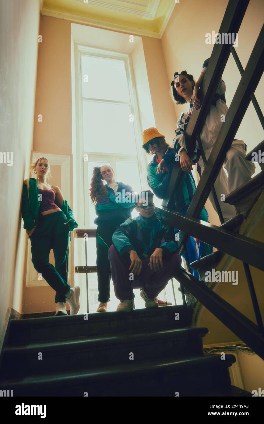 Retro-Sportswear-Trends. Junge Jungen und Mädchen, Freunde, die bunte Sportbekleidung im Stil der 90er Jahre tragen, posieren auf Treppen, Eingangsbereich. Stockfoto