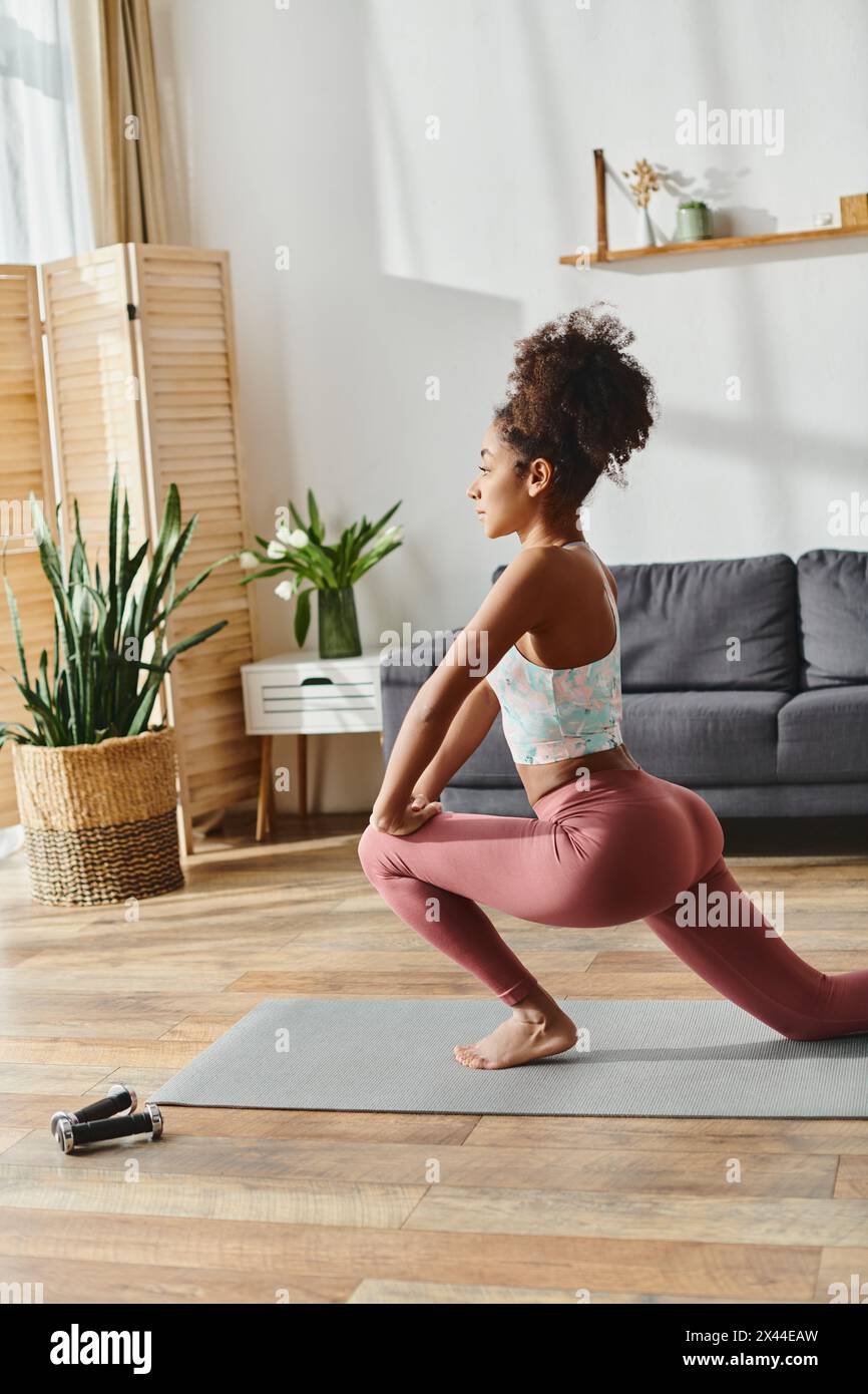 Eine lockige afroamerikanische Frau in Aktivkleidung übt Yoga in ihrem gemütlichen Wohnzimmer, das mit natürlichem Licht gefüllt ist. Stockfoto