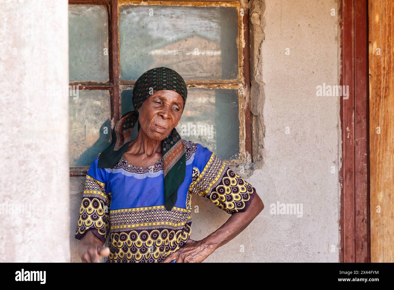 afrikanisches Dorf, alte Frau vor dem Stadthaus bei Sonnenuntergang, informelle Siedlung Stockfoto