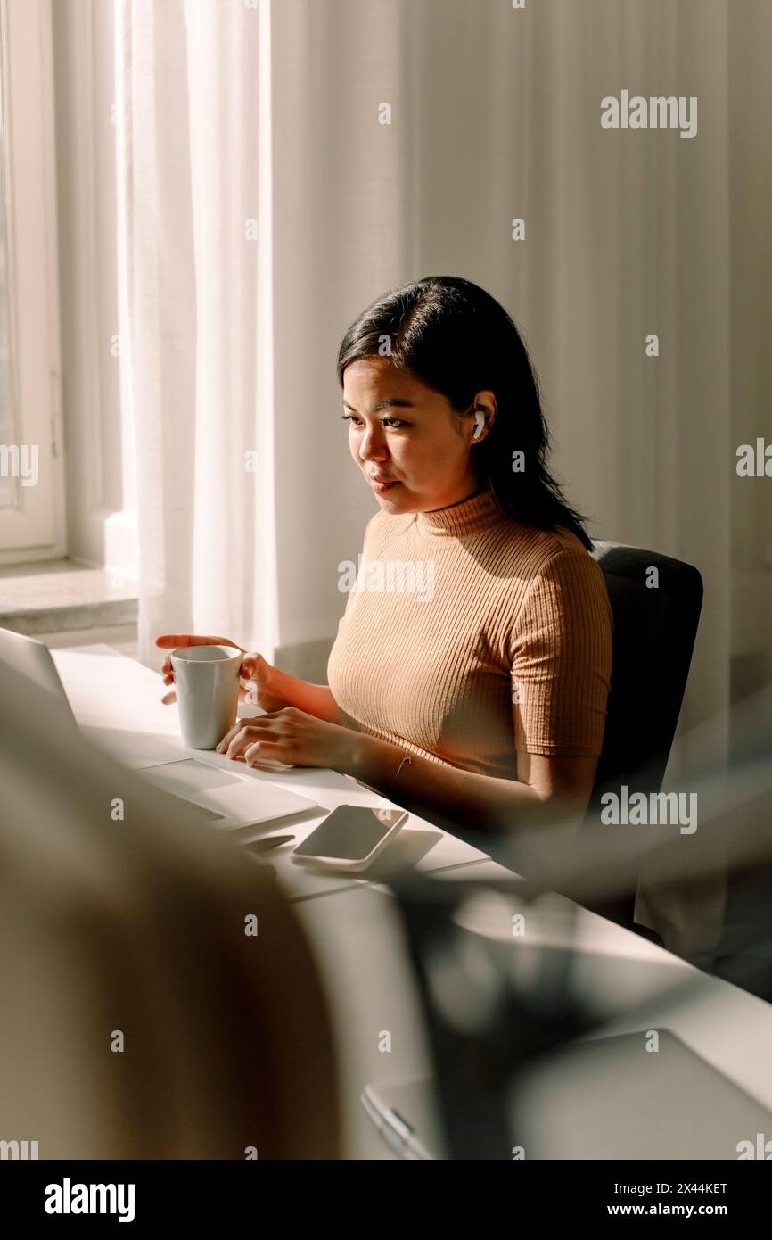 Selbstbewusste Geschäftsfrau mit Kaffeetasse und Laptop im Büro Stockfoto