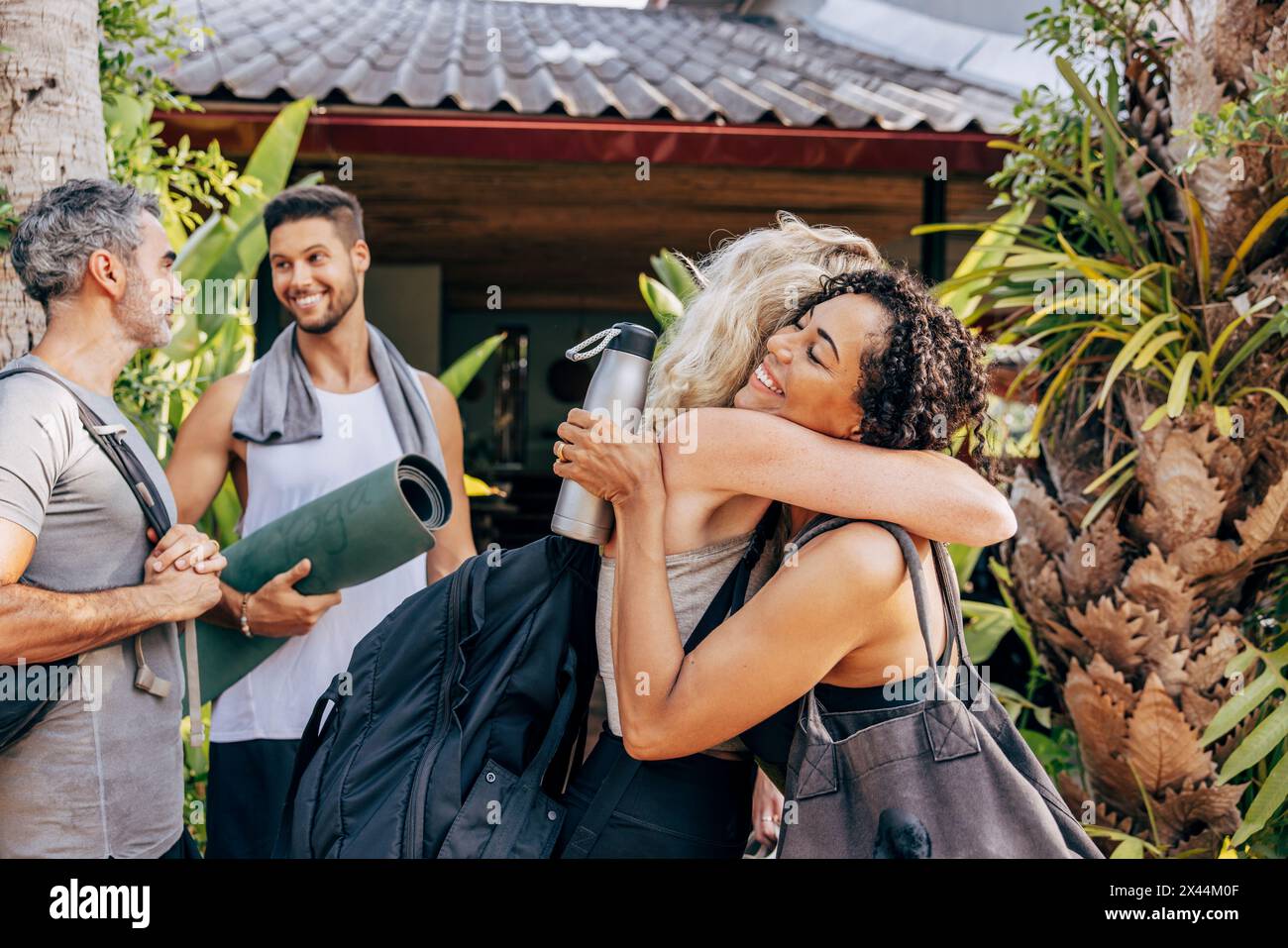 Glückliche Frauen, die sich umarmen, während sie mit männlichen Freunden vor dem Wellnessresort stehen Stockfoto