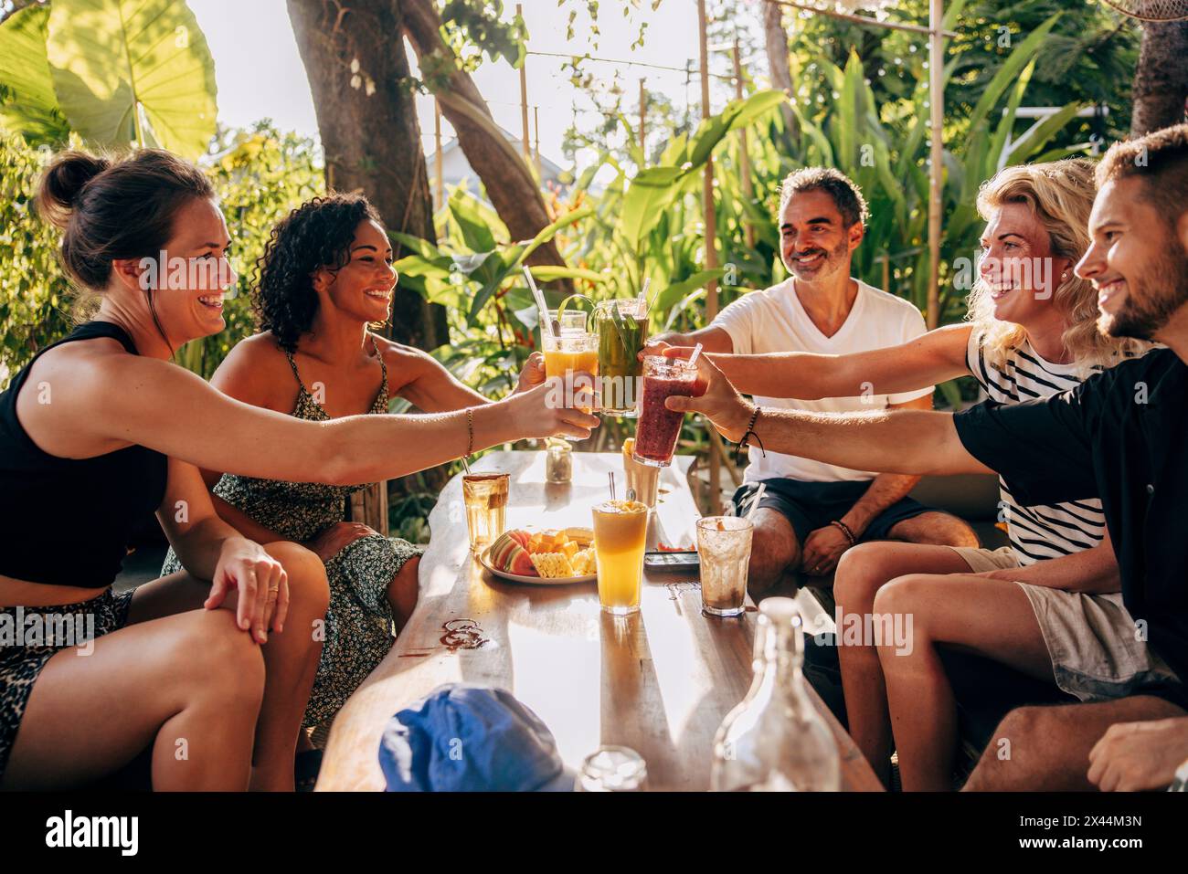 Lächelnde multirassische Freunde, die gesunde Getränke trinken, während sie im Wellnessresort sitzen Stockfoto