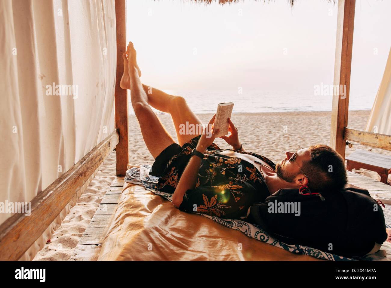 Ein Mann liest Buch, während er sich in der Cabana im Urlaub am Strand liegend Stockfoto