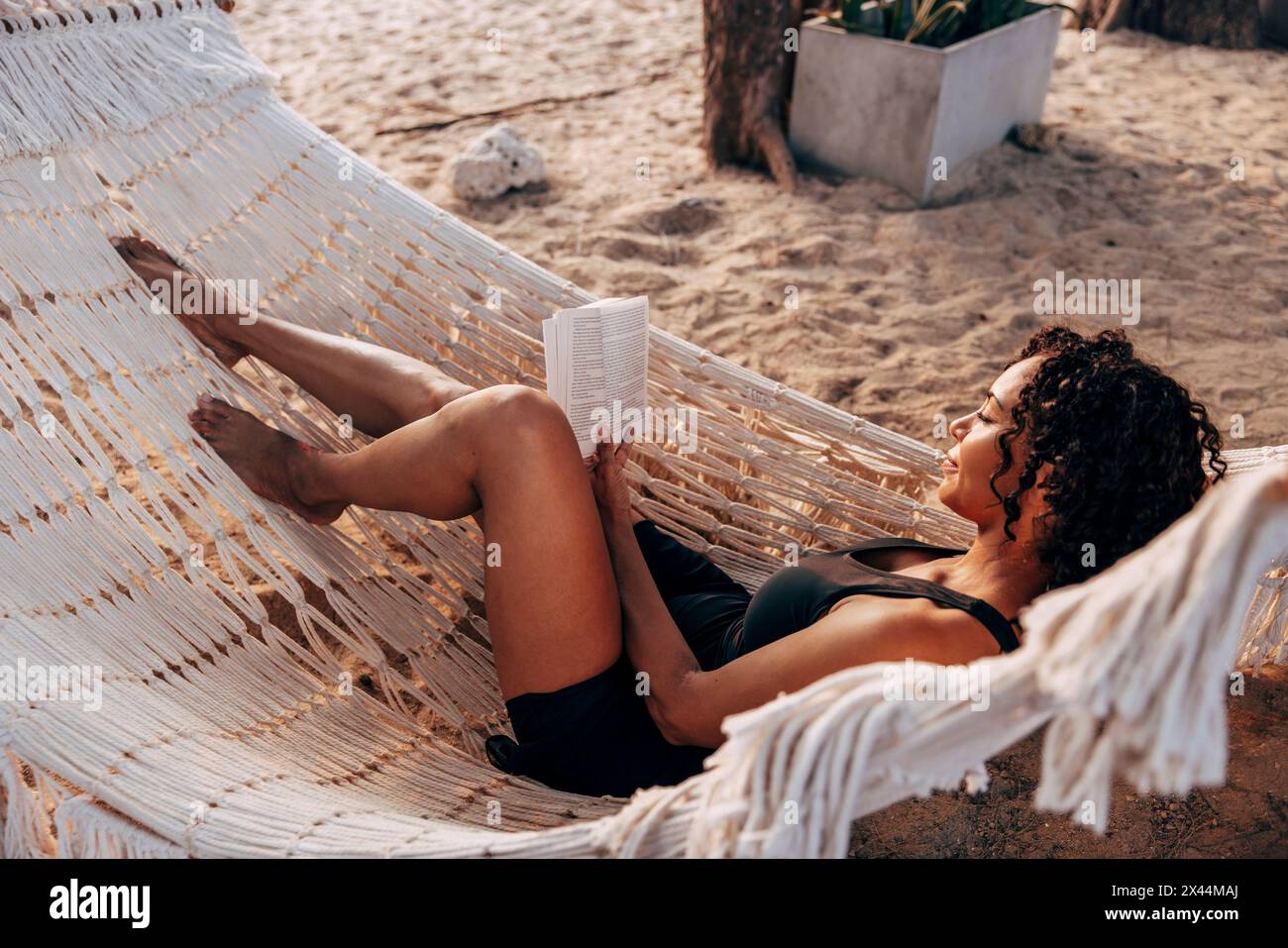 Eine Frau, die Buch liest, liegt in der Hängematte im Urlaub am Strand Stockfoto