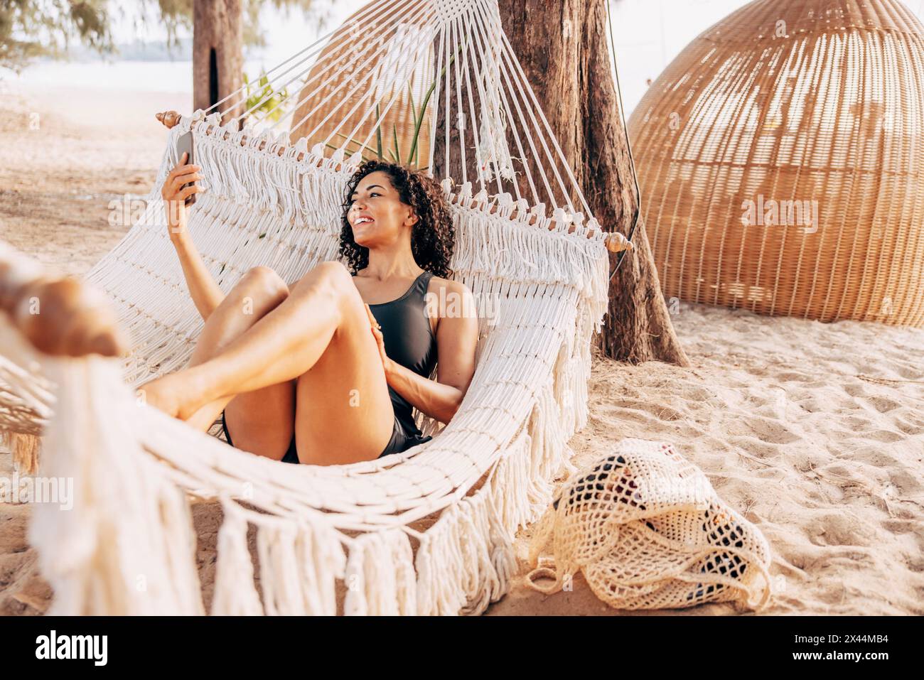 Lächelnde Frau, die Video auf dem Smartphone macht, während sie sich in der Hängematte am Strand liegend Stockfoto