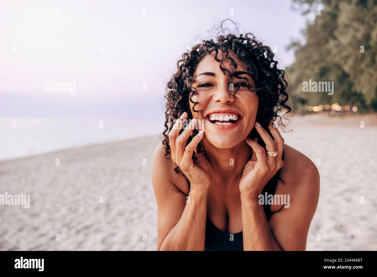 Porträt einer glücklichen Frau, die lockiges Haar zeigt, während sie Spaß am Strand hat Stockfoto