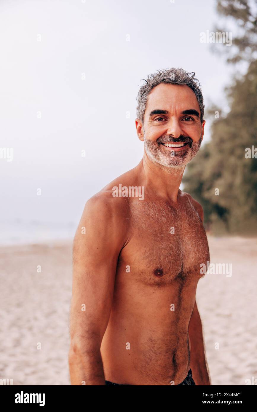 Porträt eines lächelnden, hemmungslosen Mannes, der im Urlaub am Strand steht Stockfoto