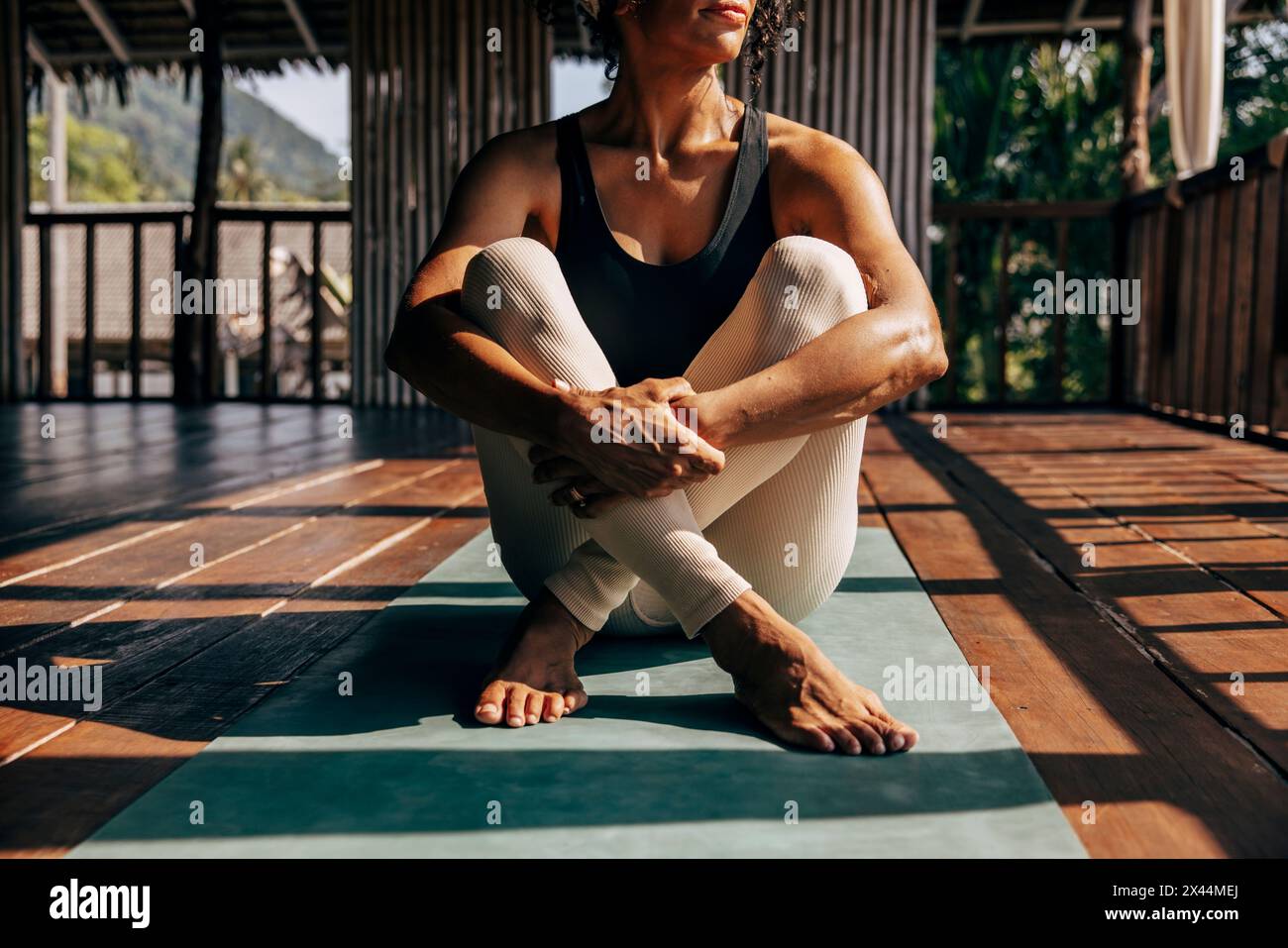 Niedriger Teil der Frau, die sich in den Knien umarmt, während sie auf einer Yogamatte im Wellnessresort sitzt Stockfoto