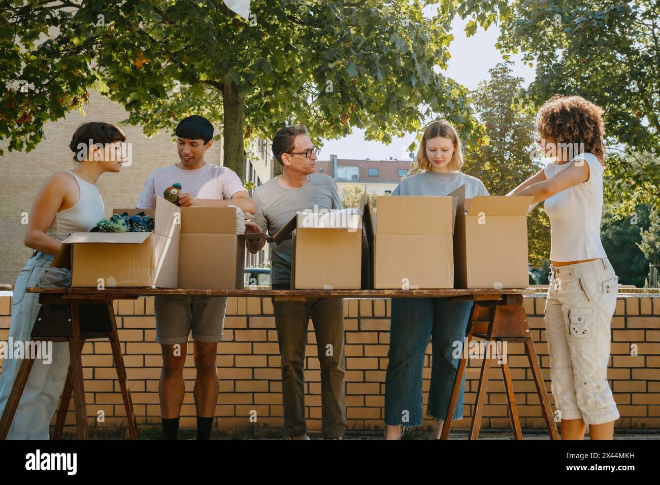 Gruppe von Freiwilligen aus verschiedenen Rassen, die sich gegenseitig helfen, während sie Boxen auf dem Tisch während der Wohltätigkeitsfahrt in Community ce arrangieren Stockfoto