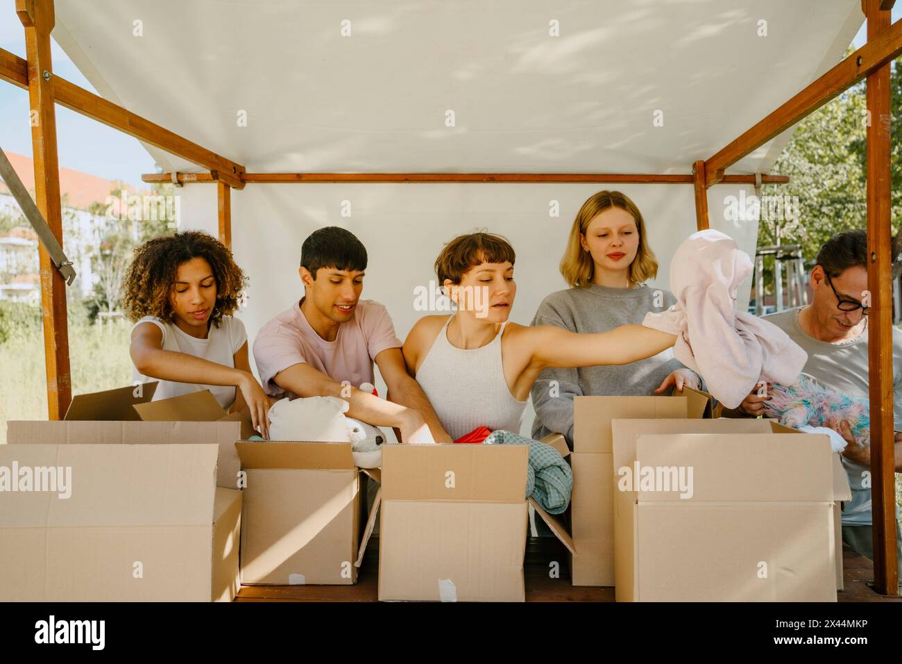 Gruppe multirassischer Freiwilliger, die Spendenwaren in Kisten unter dem Zelt im Gemeindezentrum sortieren Stockfoto